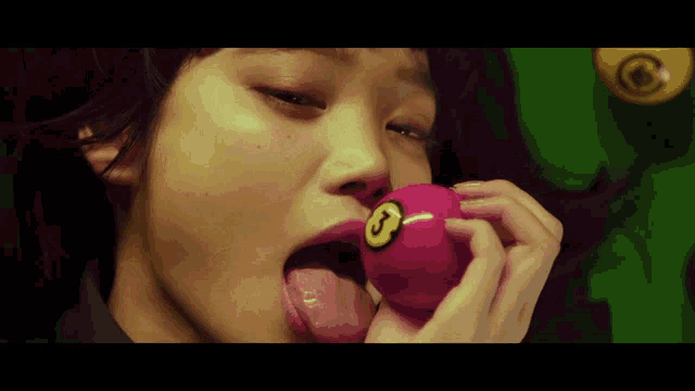 a woman licks a pink pool ball with a yellow number 8 on it