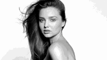 a black and white photo of a naked woman with her hair blowing in the wind .