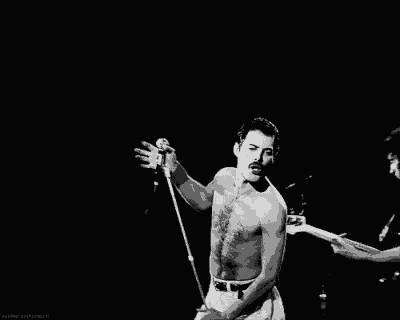 a man without a shirt is singing into a microphone on stage .