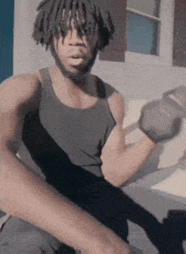 a man in a black tank top is holding a dumbbell