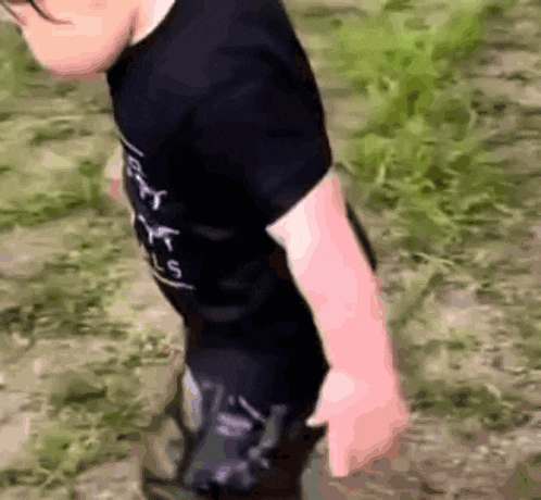 a young boy wearing a black t-shirt is standing on a grassy field .