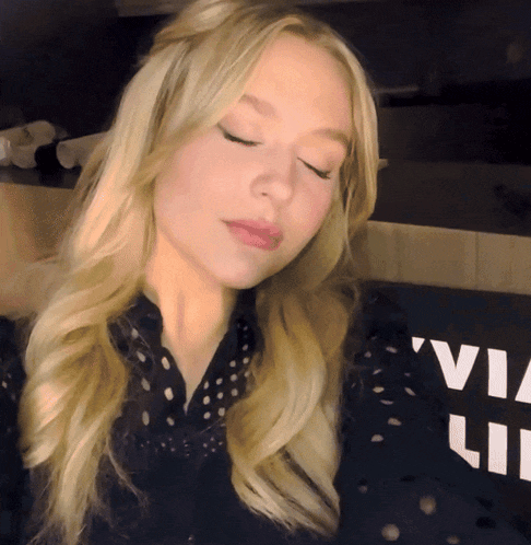 a blonde woman with her eyes closed stands in front of a sign that says via lite