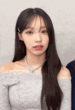 a woman wearing a gray off the shoulder top and a necklace