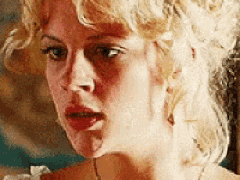 a close up of a woman 's face with blonde curly hair and a necklace .