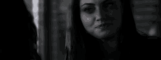 a black and white photo of a woman in a dark room looking at the camera .