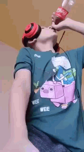 a person wearing a shirt with a pig on it is drinking a coca cola bottle .