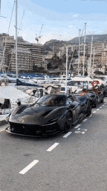 a row of black sports cars are parked on the side of the road near a marina