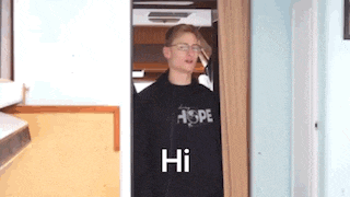 a young man wearing glasses is standing in a doorway and says hi .
