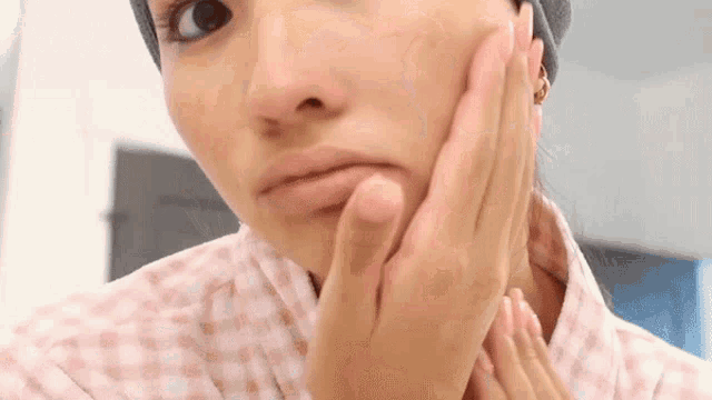 a woman looks at her face in a mirror with her hands on her face