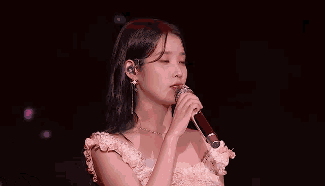 a woman in a pink dress is singing into a microphone and waving her hand