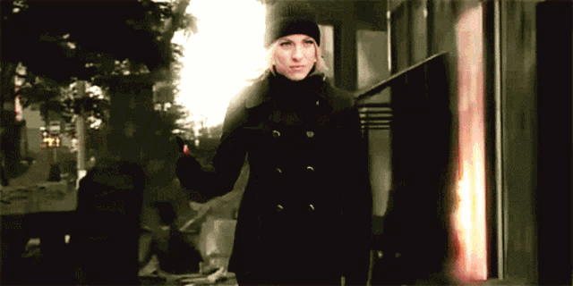 a woman in a black coat and black hat is standing in front of a building