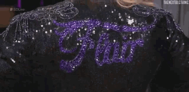 a woman is wearing a black jacket with purple sequins on the back and the word fire embroidered on it .