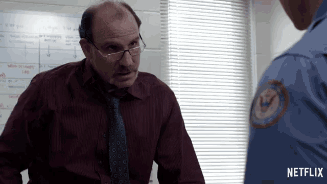 a man with glasses and a mustache is talking to a police officer with a netflix logo in the corner