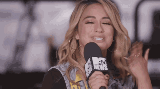 a woman speaking into a mtv news microphone with her eyes closed