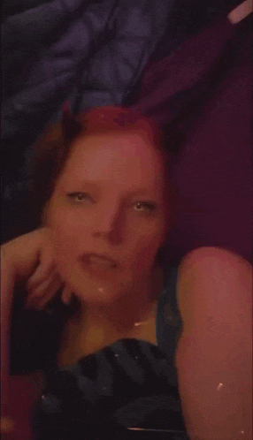 a woman with red hair is laying on a bed with a purple background