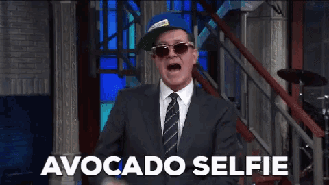 a man in a suit and tie is wearing sunglasses and a hat and the caption says avocado selfie