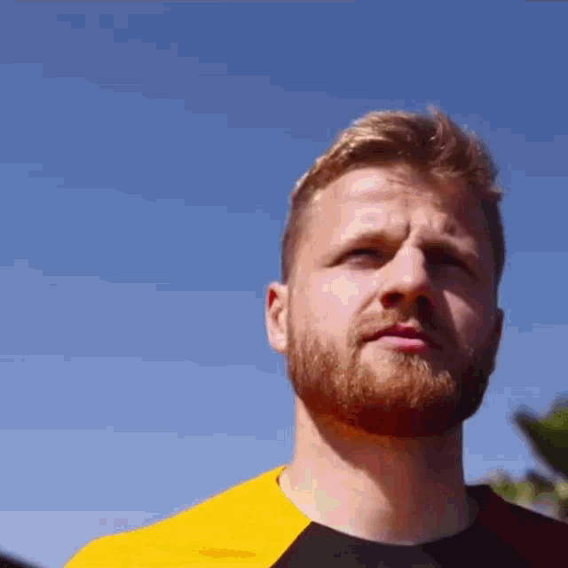 a man with a beard is wearing a yellow and black shirt against a blue sky