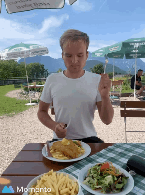 a man sitting at a table with a plate of food and a green umbrella that says wieninger bier