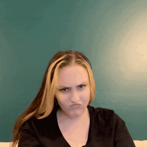 a girl with blonde hair is making a funny face in front of a green wall