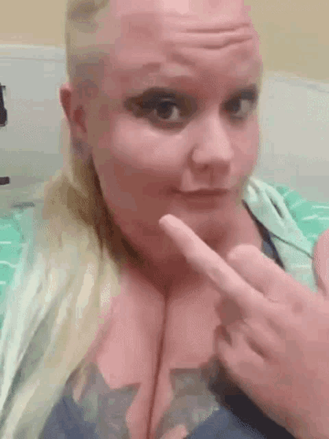 a woman with a shaved head and a tattoo on her chest is pointing at her breasts .