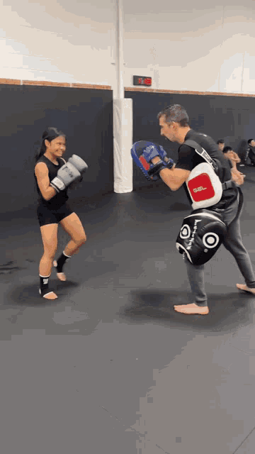 a man and a woman are boxing in a gym with a digital clock behind them that reads 9:12