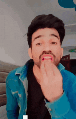 a man with a beard wearing a blue denim jacket is licking his lips
