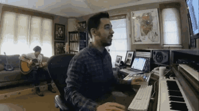 a man is playing a guitar while another man is playing a keyboard in a living room