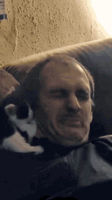 a man laying on a couch with a cat laying on his face