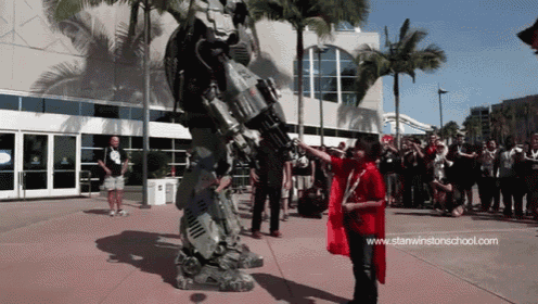 a boy in a red cape stands in front of a robot with the website www.stanwinstonschool.com visible