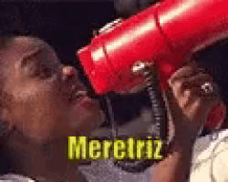 a person is blow drying their hair with a red hair dryer and the word meretriz is on the bottom of the picture .