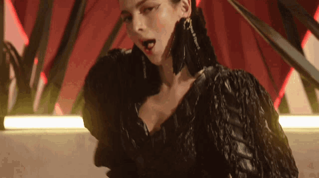 a woman in a black dress and earrings is dancing in a dark room .