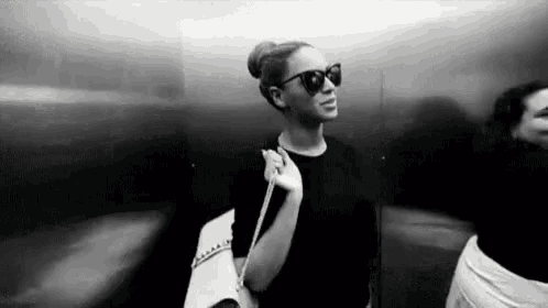 a black and white photo of a woman wearing sunglasses and a bun .