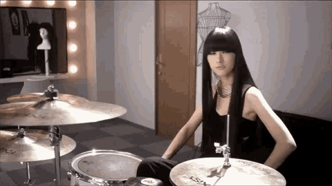 a woman is playing drums in a room with a mannequin on the wall
