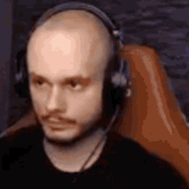 a bald man wearing headphones is sitting in a chair and looking at the camera .
