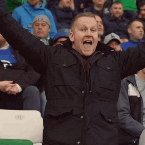 a man with his arms in the air wearing a jacket with a la hat on