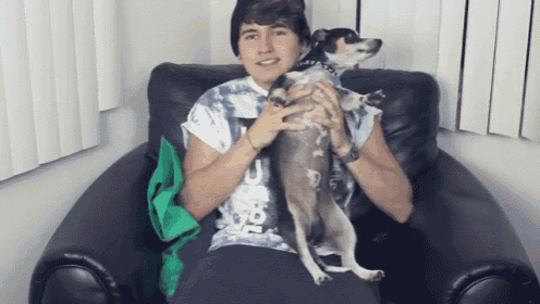 a man in a tie dye shirt is holding a small dog in his lap
