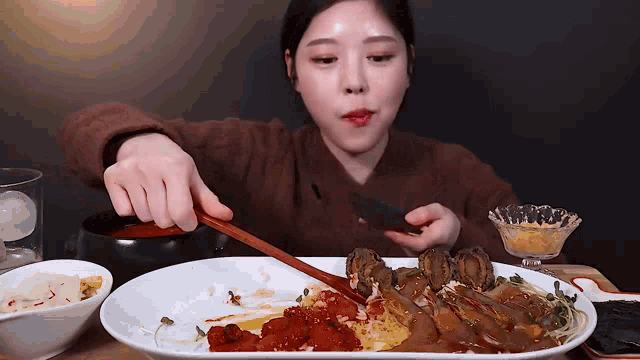 a woman is sitting at a table eating a plate of food with chopsticks .