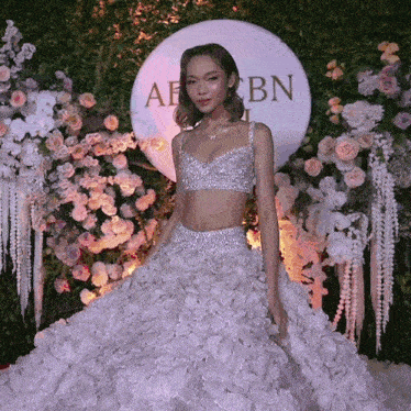 a woman in a white dress stands in front of a sign that says abn on it