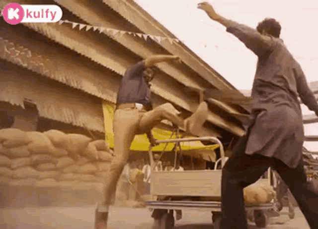 a man is kicking another man in the face while standing next to a cart with a person on it .