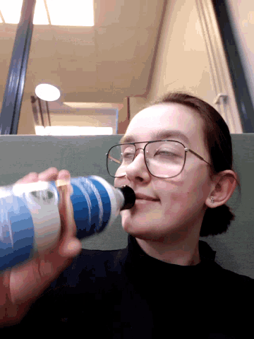a person with glasses is drinking from a bottle that says ' water ' on it