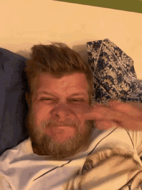 a man with a beard is laying in bed making a face