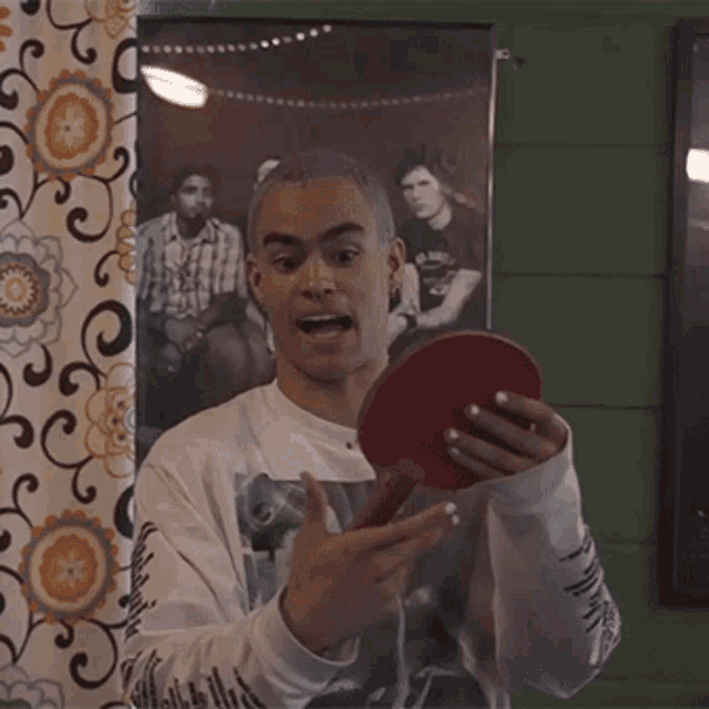 a man holding a ping pong paddle in front of a picture of a band