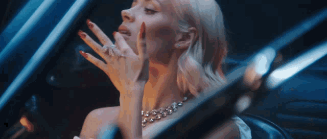 a woman with red nails and a diamond necklace is sitting in a car