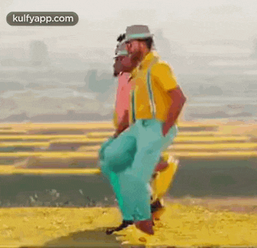 a man in a yellow shirt is dancing in a field with another man .