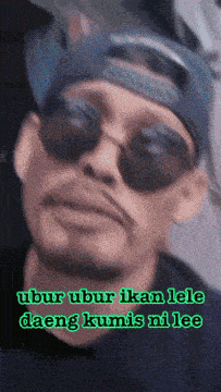 a man wearing sunglasses and a hat with the words " ubur ubur ikan lele daeng kumis ni lee " below him