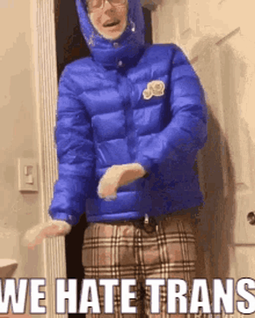 a person wearing a blue jacket and plaid pants is standing in front of a door and saying we hate trans .