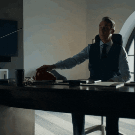 a man in a suit and tie is sitting at a desk with his arm outstretched