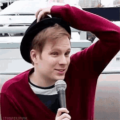 a man wearing a hat and a red sweater is holding a microphone and scratching his head .