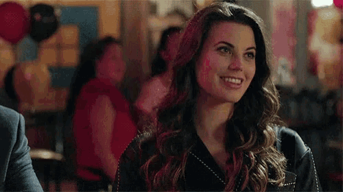 a woman is smiling while sitting at a table in a room with balloons in the background .