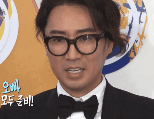 a man wearing glasses and a bow tie has a foreign language behind him